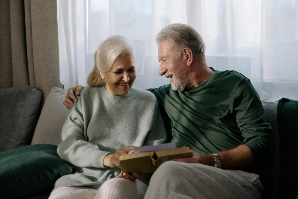 Adultos mayores sentados en un sofá leyendo y sonriendo. Pañales para adultos calzón desechable para adulto - Evita llagas en la piel de adultos mayores 